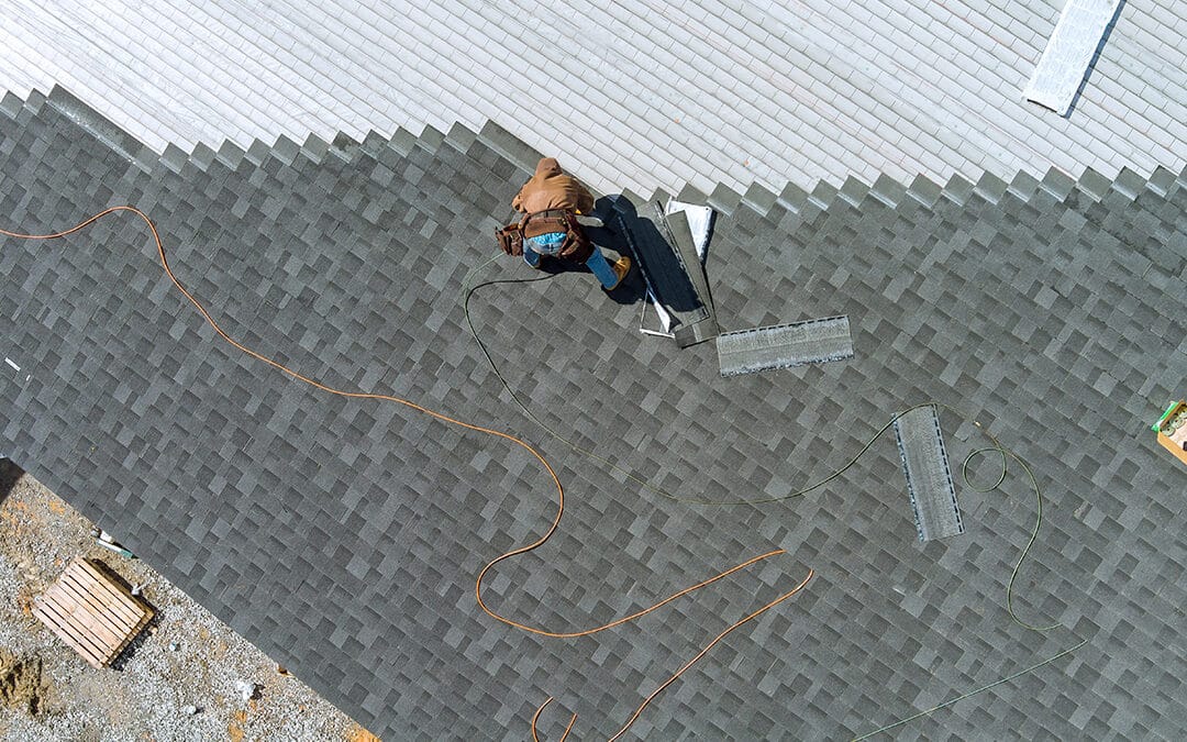 Drone view of a worker installing shingles on a roof, showcasing the roofing installation process and skilled craftsmanship.