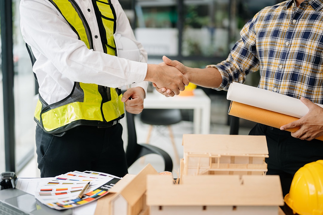 Construction team shake hands greeting start new project plan behind yellow helmet on desk in office center to consults about their building project.